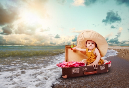 Funny baby girl traveler sitting in retro suitcase at the sea coastの写真素材