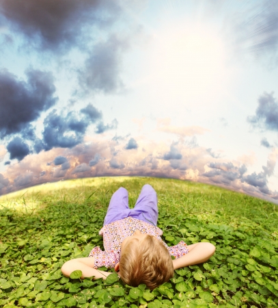 Carefree little boy lying on the green grass under blue skyの写真素材