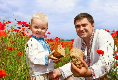 Father and little son with bread on the poppies fieldの写真素材