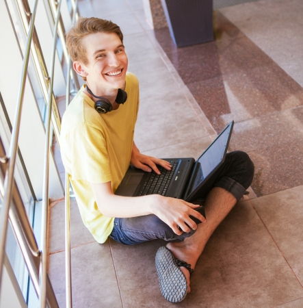 Handsome teenage boy sitting on the floor of commercial center with notebookの写真素材