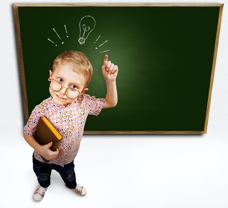 Little boy with eurica gesture standing near green schoolboardの写真素材