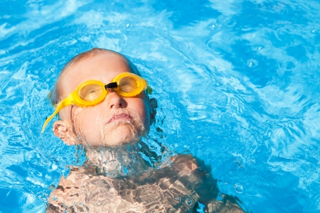 Little boy in yellow goggles swims on his backの写真素材