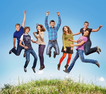 Group of teens jumping in the blue sky above the green grassの写真素材