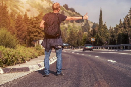 Hitchhiking traveler try to stop car on the mountain roadの写真素材