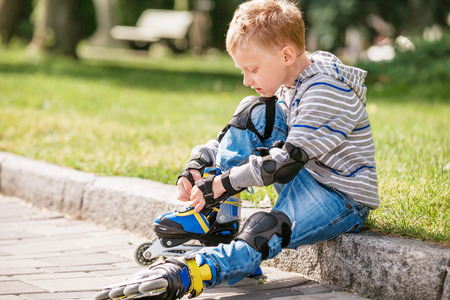 Little boy lace his roller skate sitting on the sidewalkの写真素材