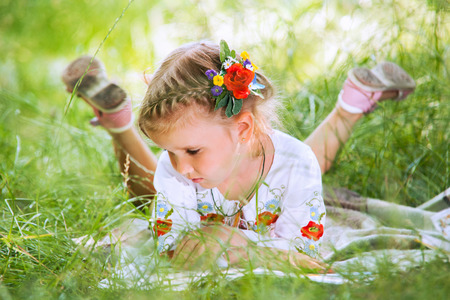 Little girl reading tales lying in green grassの写真素材