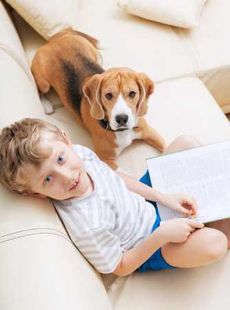 Boy reading tales for his dog at homeの写真素材