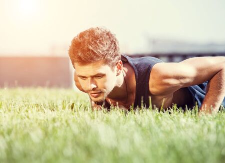 Push up muscular man on green lawn in city parkの写真素材