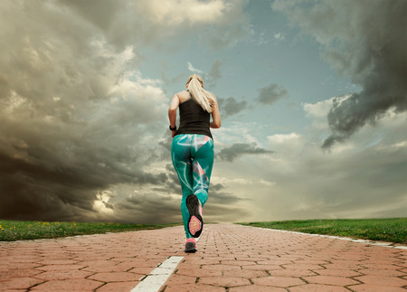 Young blonde girl evening jogging with great cloudscapeの写真素材