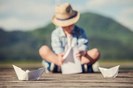Boy make a paper boat sitting on the wooden pierの写真素材