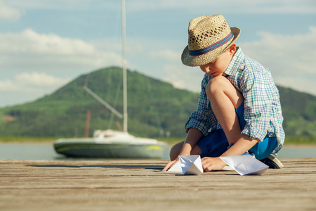 Little boy make paper boats sitting on the wooden pierの写真素材