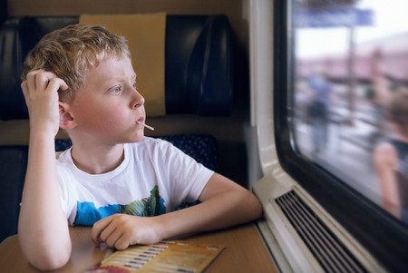 Bored boy with candy look in train windowの写真素材
