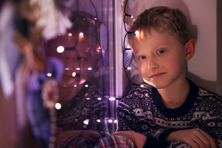 Calm little boy on the windoe with Christmas Lightsの写真素材