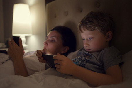 Mother with son lying in bed and look in their electronic deviceの写真素材