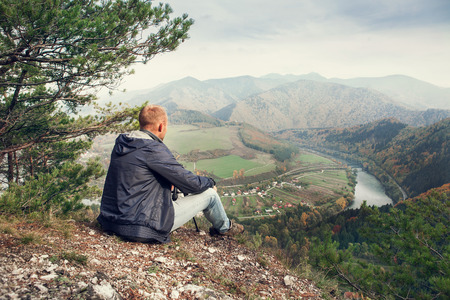 Man sitting on the edge of the cliff above mountaine valleyの写真素材