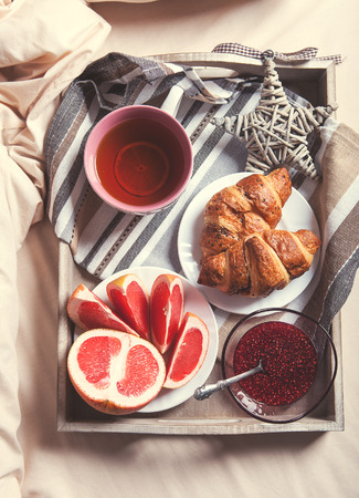 Cup of fresh tea and croissants into service tray on the bedの写真素材