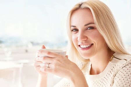 Pretty young woman with cup of coffee in sunny restarauntの写真素材
