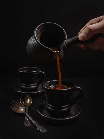 Men hand pouring the coffee in clay cup: black on the blackの写真素材