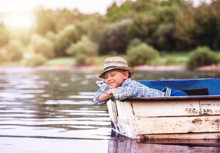 Little boy in old boat on the calm lake surfaceの写真素材