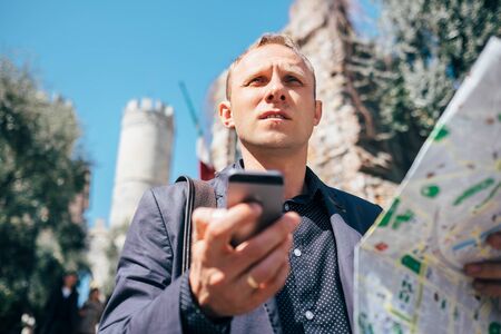 Tourist man try navigate himself with map and smartphone in unknown cityの写真素材