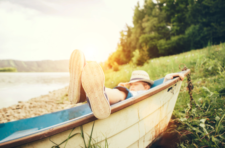 Boy lying in old boat near the lakeの写真素材
