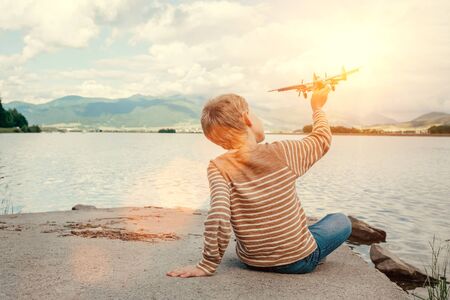 Boy play with toy plane sitting near the lakeの写真素材