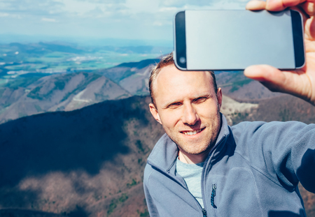Man take self photo with smartphone on the top of mountainの写真素材