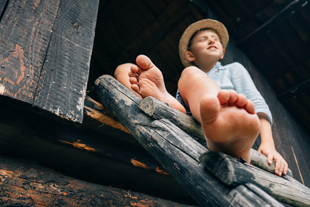 Barefoot boy sits on barn ladderの写真素材