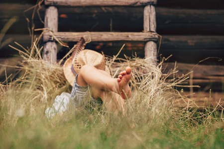 Barefoot boy sleeps on the grass near ladder in haystackの写真素材