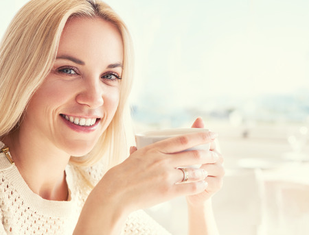 Pretty young woman with cup of coffee in sunny restarauntの写真素材