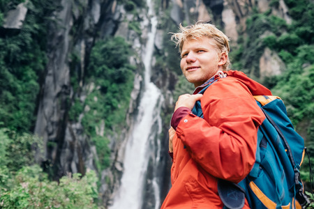 Young man with backpack near the waterfallの写真素材
