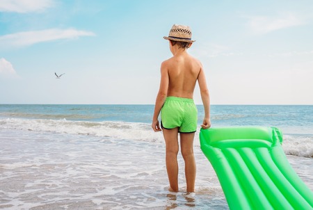 Boy stands with swimming air mattress on the sea surf lineの写真素材