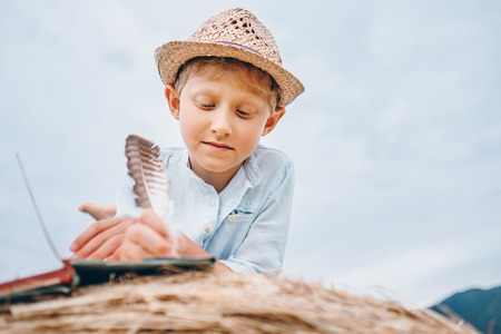  Boy writes a notes with feather lying on hay roll