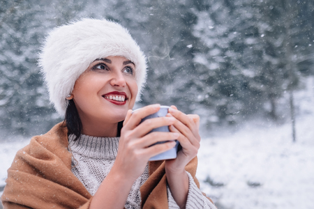 Woman with cup of hot tea on snowy forest backgroundの写真素材