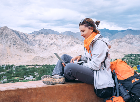 Backpacker with laptop sits on the top view point under mountain settelmentの写真素材