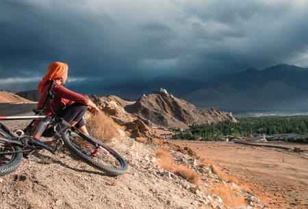 Woman bicycle traveler looking to Ladakh mountain range, Indiaの写真素材