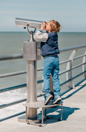 Boy try to looks in binocular on the sea pierの写真素材