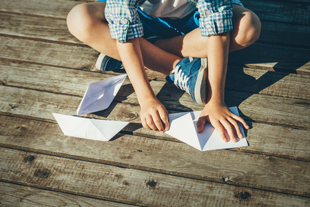 Boy makes paper boats on wooden pier - close up hands and legs imageの写真素材