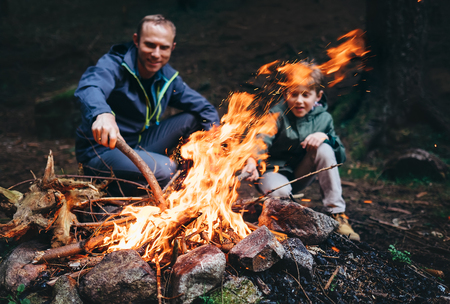 Father and son make bonfire in forest. Camping trip at spring or autumn time. Family relationship concept imageの写真素材