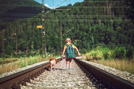 Little boy with big backpack and his beagle dog run on the railwayの写真素材