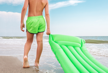 Boy with green swimming mattress stands on seasurf lineの写真素材