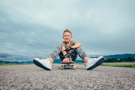 Boy sitting on skateboard on asphalt roadの写真素材