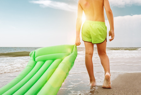 Boy with green swimming mattress stands on seasurf lineの写真素材