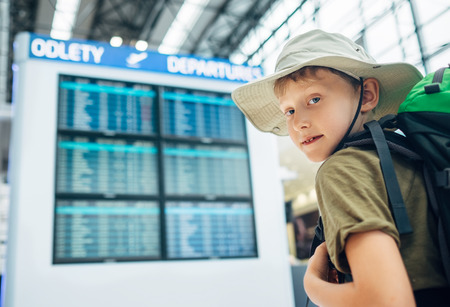 Boy ready for journey near the departure information desk in airportの写真素材
