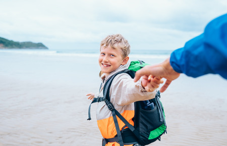 Happy smiling boy holds his father on hand and runs to the surf ocean lineの写真素材