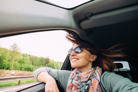 Woman with flying hair looks from car windowの写真素材