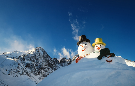 Snowman family under blue sky in winter mountainの写真素材