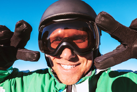 Skier dressed in ski helmet and ski goggles showing the two victory gestures portrait