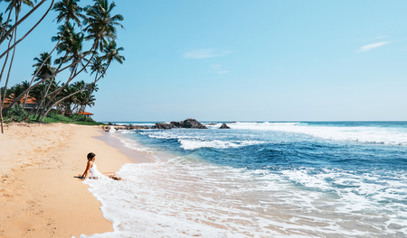 Woman enjoy with ocean surf sitting on the lonely tropical beach under the palm treesの写真素材