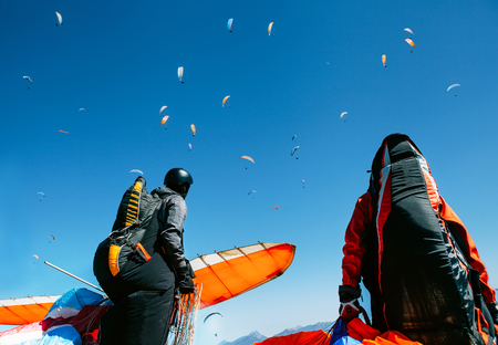 Two paragliders with full flight equipment look on soaring another paragliders in skyの写真素材